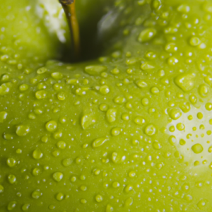 Close up of a ripe green apple with a few drops of water glistening on its surface.